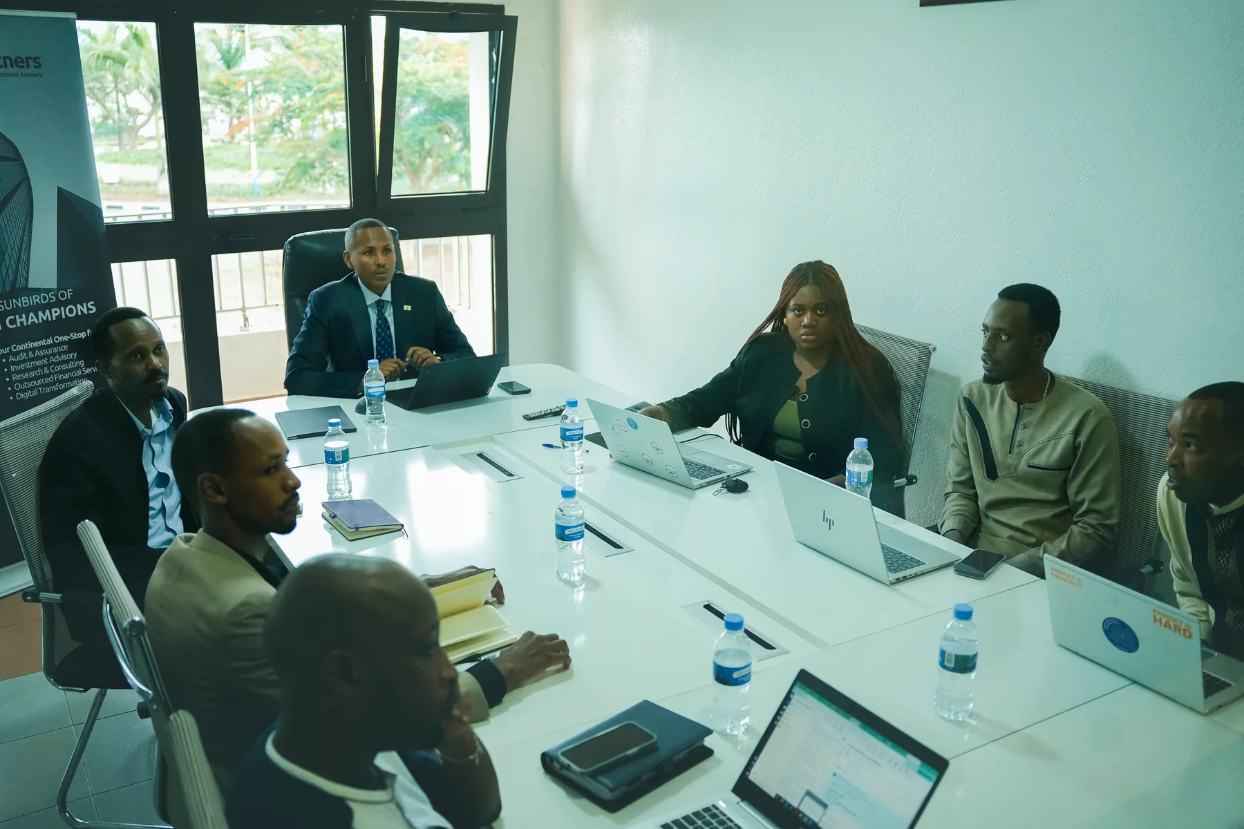 A working session around a meeting table, with a Sunbirds banner in the background